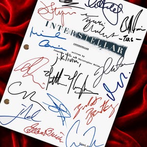 May include: A white script cover page for the film Interstellar, written by Jonathan Nolan and Christopher Nolan, featuring numerous signatures in black, blue, and red ink. The document has three metal binder holes along the left side.