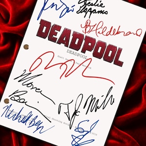 May include: A white script with the word "DEADPOOL" in red block letters, surrounded by multiple signatures in blue, black, and red ink. The script is on a red velvet background.