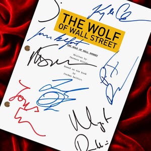 May include: A white script featuring the title "THE WOLF OF WALL STREET" in black letters on a yellow background. The script is covered in signatures and rests on a red velvet surface.