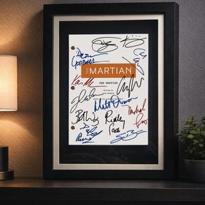 May include: A framed script cover for The Martian, featuring a white page with black, blue, and red ink signatures. The title The Martian is printed in white on an orange rectangular background. The script includes text credits and two metal binder holes.