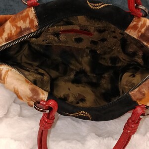 May include: Open view of a handbag with a mix of textures and colors. The bag features a patchwork design with animal print and black suede panels. Red handles and silver-tone hardware add contrast. The interior has a leopard print lining.