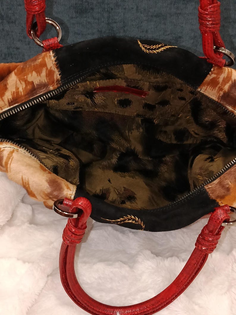 May include: Open view of a handbag with a mix of textures and colors. The bag features a patchwork design with animal print and black suede panels. Red handles and silver-tone hardware add contrast. The interior has a leopard print lining.