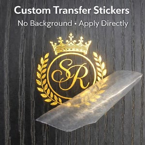 May include: A gold custom transfer sticker with a crown and laurel wreath design, featuring the letters "SR" inside a circle. The sticker is shown on a dark wood grain surface. Text reads "Custom Transfer Stickers. No Background • Apply Directly."