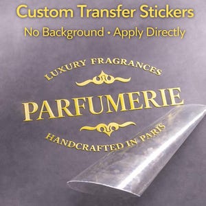 May include: Gold-coloured custom transfer stickers with the text "Custom Transfer Stickers, No Background, Apply Directly". The stickers also read "Luxury Fragrances, Parfumerie, Handcrafted in Paris". A clear sheet is partially peeled back.