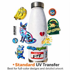 May include: A white metal water bottle decorated with various colorful stickers including a holographic fox, a bunch of bananas, a broken heart, a ninja character, and a name tag sticker that reads Hello, I'm DTF, with text below reading Standard UV Transfer.