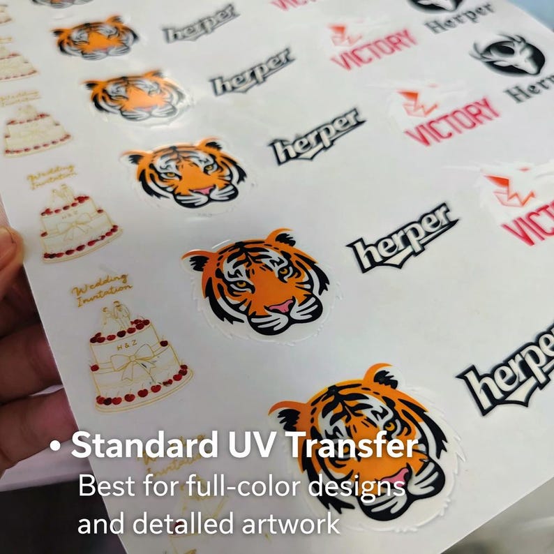May include: A sheet of stickers featuring tiger faces, wedding cake designs, and logos. The tiger stickers are orange and black. Text on the sheet includes "Herper", "Victory", and "Wedding Invitation". The text "Standard UV Transfer" is also visible.