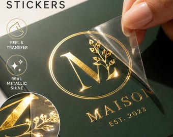 May include: Foil transfer stickers with a gold metallic shine. The stickers are being peeled from a dark green surface. The design includes the word "MAISON" and the year "EST. 2023" in gold. The stickers are for a variety of uses.