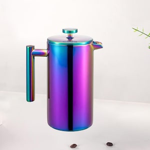 Op de afbeelding: Een roestvrijstalen French press koffiezetapparaat met een levendige, iriserende afwerking. De kleuren verschuiven van blauw naar paars en groen. Het heeft een handvat, een deksel met een kleine knop en een tuit. Twee koffiebonen staan op de voorgrond.