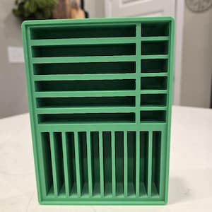 May include: A bright green organizer with multiple compartments and slots. The rectangular container has horizontal and vertical dividers, creating various storage spaces. The design suggests it's for organizing small items.