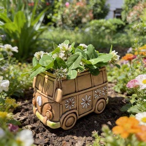 May include: A ceramic planter shaped like a vintage van, painted in shades of tan and brown, with white daisy and peace sign details. The van is filled with green clover and white flowers, set in a garden setting.