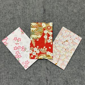 以下が含まれることがあります： 花柄の装飾紙の長方形の3つの部分。中央の作品は、白い花と金のアクセントが付いた赤色です。他の2つの作品は、白い背景にピンクと白の花柄のデザインがあります。