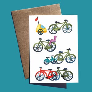 May include: Greeting card featuring watercolor illustrations of bicycles in various styles and colors, including green, red, and blue. One bicycle has a yellow trailer. The card is paired with a brown envelope.