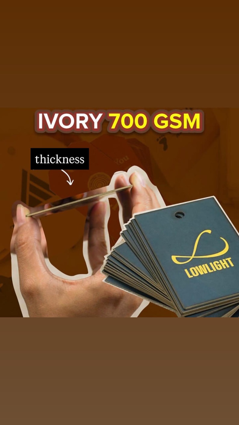 May include: A stack of square dark blue hang tags with a gold logo and the text LOWLIGHT, alongside a single tag held up to show its ivory 700 GSM thickness. The tags feature a small hole at the top for attachment, showcasing a sturdy paper quality.