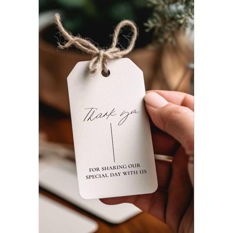 May include: A rectangular off-white paper tag with rounded top corners, featuring a jute twine loop. The text reads Thank you in a script font above a vertical line, with the text FOR SHARING OUR SPECIAL DAY WITH US in a sans-serif font below.