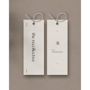May include: Two rectangular off-white paper tags with rounded corners and a hole at the top, each threaded with a thin string. The left tag features the text the recollective, while the right tag displays the letter R and additional small text.