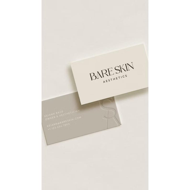 May include: Two rectangular business cards. The top card is cream-colored with black text reading BARE SKIN AESTHETICS. The bottom card is light gray with white text including the name Keianh Race, title Owner & Aesthetician, email, and phone number.