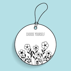 May include: A white, round tag with the text "CHOOSE YOURSELF" in black. The tag features a black floral design at the bottom and a black string for hanging. The background is a light blue.