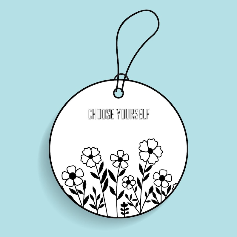 May include: A white, round tag with the text "CHOOSE YOURSELF" in black. The tag features a black floral design at the bottom and a black string for hanging. The background is a light blue.