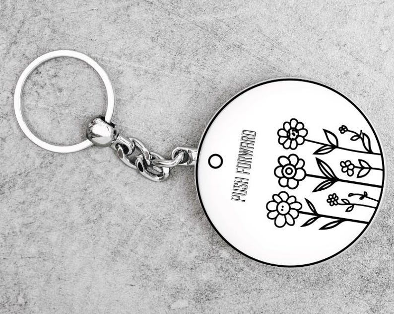 May include: A round, white keychain with a black floral design and the words "PUSH FORWARD." The keychain has a silver chain and ring. The design features three flowers and several leaves.
