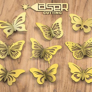 Puede incluir: Nueve decoraciones de mariposas amarillas cortadas con láser con intrincados diseños de alas están dispuestas sobre una superficie de madera. Las palabras "LASER CUTTING" se muestran en oro sobre las mariposas. Estas mariposas decorativas son ideales para proyectos de manualidades.