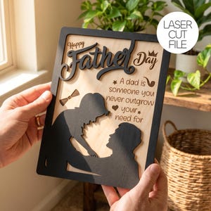 Peut inclure: Panneau en bois pour la fête des pères avec un cadre noir. Le panneau comporte les mots "Happy Father's Day" et une silhouette d'un enfant et d'un père. Le texte "A dad is someone you never outgrow your need for" est également inclus.