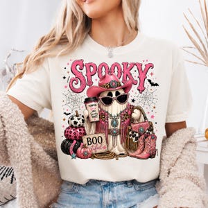 Western cowgirl Halloween design displayed on a shirt with a turquoise glam ghost, leopard-print details, spiderwebs, pumpkins, western accessories, and spooky typography.