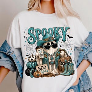 Western cowgirl Halloween design displayed on a shirt with a turquoise glam ghost, leopard-print details, spiderwebs, pumpkins, western accessories, and spooky typography.