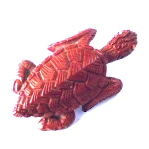 May include: A reddish-brown turtle figurine with a textured shell and detailed head and flippers. The sculpture is set against a white background, highlighting the intricate carving and design of the artwork.