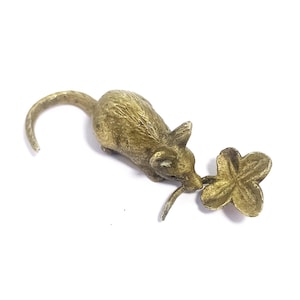 May include: A small, antique-style brass mouse figurine with a long tail and a four-leaf clover. The mouse is detailed with visible ears and whiskers, and the clover has a textured surface. The figurine is set against a white background.