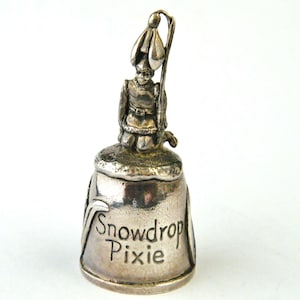 May include: Silver bell with a snowdrop pixie figurine on top. The bell is inscribed with the words "Snowdrop Pixie".