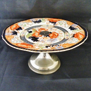 May include: A vintage cake stand with a silver base and a colourful floral patterned ceramic top.