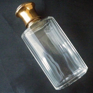 May include: A clear glass bottle with a gold metal stopper. The bottle is rectangular in shape and has a slightly rounded bottom.