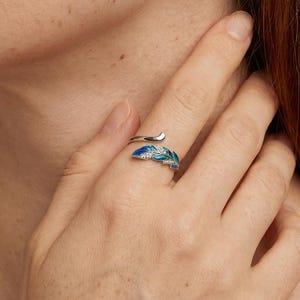 May include: Silver ring and earrings set with a feather design. The ring wraps around the finger, and the earrings dangle. The feather design features shades of blue and white enamel. Jewellery.