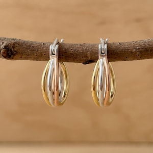 May include: A pair of hoop earrings featuring a tri-color design with interlocking bands of yellow gold, white gold, and rose gold. Each earring has a hinged post mechanism at the top, creating a rounded, teardrop-like shape with a polished finish.