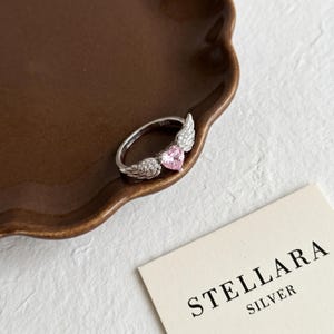 Sterling silver heart ring featuring a sparkling heart cut cz stone wrapped in two angel wings, a minimalist ring and dainty silver ring for women that doubles as a thoughtful promise ring, anniversary ring, statement ring or friendship ring for daily wear or romantic gifting.