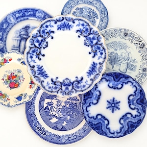 May include: A collection of six ceramic plates featuring various blue and white transferware patterns, including floral motifs, landscape scenes, and a fruit basket design, arranged in an overlapping circular composition.