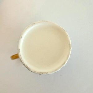 May include: An overhead shot of a ceramic mug with a cream-coloured interior and a tan handle. The rim of the mug shows signs of wear, with small chips and discolouration. The mug is set against a plain white background.