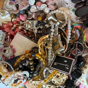 May include: A jumble of jewellery items, including necklaces, bracelets, earrings, and brooches. The collection features beads, pearls, metal, and gemstones in various colours and styles. There is a watch and a peace sign pendant. A diverse selection of accessories.