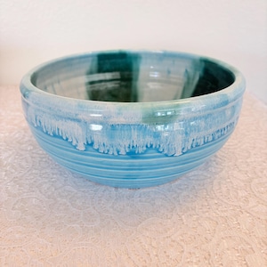 May include: A ceramic bowl with a glossy, turquoise exterior. The bowl features a textured, ridged design on the lower half and a dripped white glaze effect around the rim. The interior has a teal and white color scheme.
