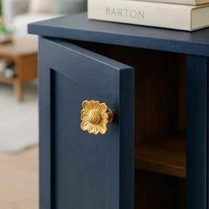 May include: A navy blue cabinet with a partially open door. The cabinet has a gold-coloured, flower-shaped knob. The word "BARTON" is visible on the spine of a book on top of the cabinet.