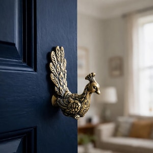 Peut inclure: Une poignée de porte en laiton en forme de paon, fixée sur une porte bleu foncé. La poignée est finement détaillée, représentant les plumes et la forme de l'oiseau. L'arrière-plan est flou.