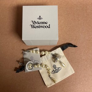 Pode incluir: Uma caixa branca com o logotipo da Vivienne Westwood est&aacute; posicionada acima de um par de brincos de p&eacute;rolas e uma pulseira a condizer. Os brincos e a pulseira t&ecirc;m um design de esfera prateada. Uma pequena bolsa branca suja com o logotipo da Vivienne Westwood tamb&eacute;m est&aacute; presente.