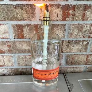 May include: A clear glass bottle with a gold top and a lit wick. The bottle is labeled "BULLEIT BOURBON FRONTIER WHISKEY" and "KENTUCKY STRAIGHT BOURBON".