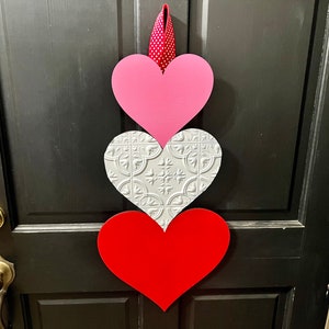 May include: A trio of wooden hearts in pink, white with a decorative pattern, and red, hanging on a black door.