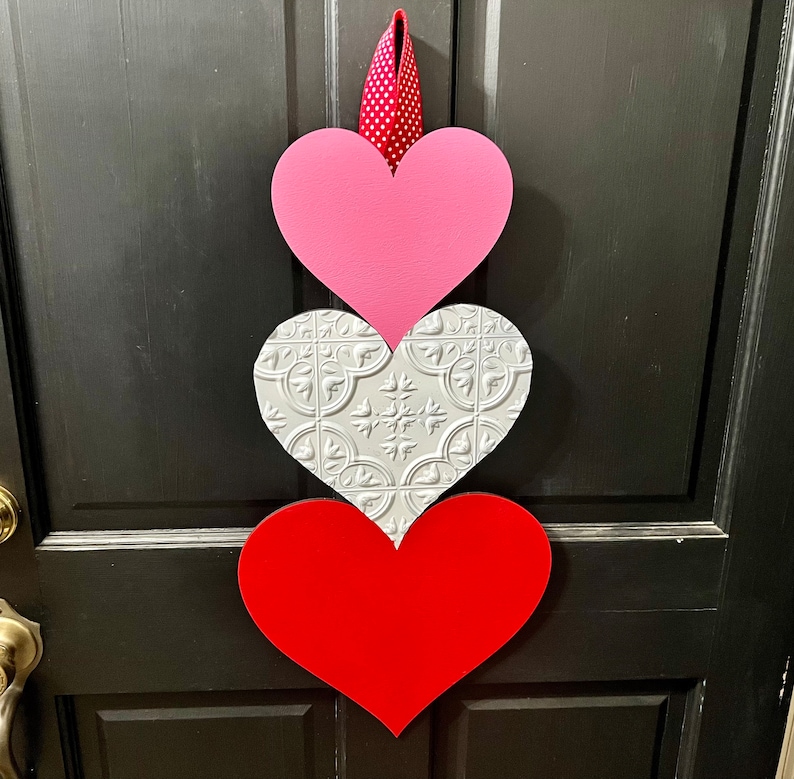 May include: A trio of wooden hearts in pink, white with a decorative pattern, and red, hanging on a black door.