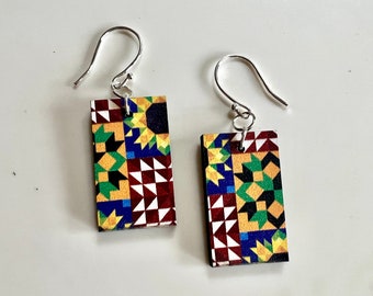 May include: A pair of silver earrings with rectangular wooden charms. The charms are covered in a colorful geometric pattern with shades of red, yellow, green, blue, and black.