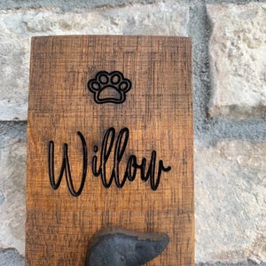 Op de afbeelding: Een houten hondenriemhaak met een pootprint en de naam "Willow" erop gegraveerd. De haak is in de vorm van een teckel.