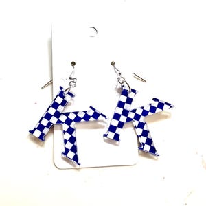 May include: A pair of earrings shaped like the letter "K". The earrings are white and blue checkered. They hang from silver-colored fish hook ear wires. The earrings are displayed on a white earring card.