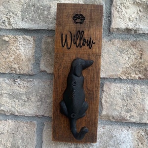 Op de afbeelding: Een houten hondenriemhaak met een zwart metalen hondensilhouet. De haak is gegraveerd met het woord "Willow" en een pootprint.