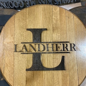 May include: A round wooden sign with the letter L and the name Landherr burned into the wood. The sign is made from a repurposed barrel.